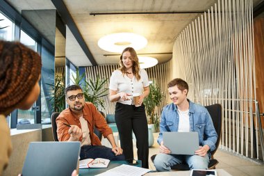 Meslektaşlardan oluşan bir ekip ve yeni başlayan profesyoneller, her biri dizüstü bilgisayarlarına odaklanarak bir proje üzerinde işbirliği içinde bir masanın etrafında toplandılar..