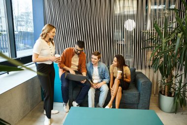 Yeni başlayan bir takımdan bir grup iş arkadaşı modern bir iş ortamında şık mavi bir kanepenin etrafında birlikte çalışırlar..