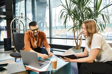 Bir erkek ve bir kadın dizüstü bilgisayarlarla aynı masada oturuyor ve ortak bir çalışma alanındaki bir girişim projesinde işbirliği yapıyorlar..
