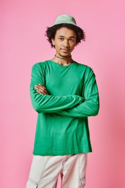 Pembe arka planda yeşil gömlek ve pantolon giyen kıvırcık saçlı neşeli, Afro-Amerikan bir adam..