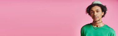 Yeşil tişörtlü genç bir Afro-Amerikalı canlı pembe arka planda poz veriyor.