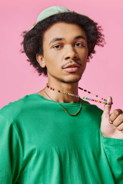Kıvırcık saçlı, yeşil tişörtlü ve pembe arka planda boncuklu kolyesi olan genç bir Afrikalı Amerikalı..