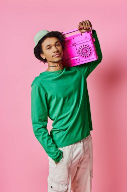 Pembe arka planda pembe bir teyp taşıyan yeşil tişörtlü, neşeli bir Afrikalı Amerikalı..