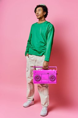 Neşeli, genç, Afro-Amerikan bir adam pembe bir müzik kutusunu canlı pembe bir arka planın önünde tutuyor..