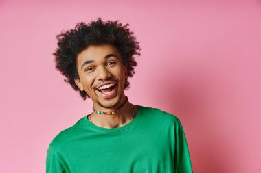 A cheerful African American man with a curly afro wearing a green shirt, expressing emotions on a pink background. clipart