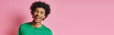 A cheerful young African American man with curly hair, wearing casual green shirt, smiling on pink background. clipart