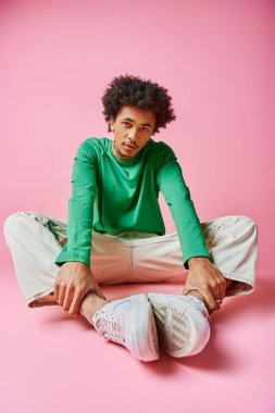 Kıvırcık saçlı, sıradan giyinmiş, derin düşüncelere dalmış, çapraz bacaklı bir şekilde yerde oturan Afro-Amerikan bir adam..