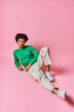 Neşeli, kıvırcık, sıradan giyinmiş Afro-Amerikan bir adam coşkulu bir şekilde pembe bir arka planda dinleniyor..
