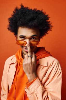 A young African American man with curly hair donning an orange shirt, jacket, and sunglasses against an orange backdrop, showcasing a vibrant and eclectic style. clipart