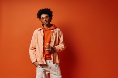 Havalı, turuncu ceketli ve turuncu arka planda beyaz pantolonlu Afro-Amerikan bir adam..