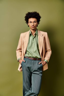Şık, kıvırcık, takım elbiseli ve kravatlı genç bir Afro-Amerikalı canlı yeşil bir duvarın önünde duruyor..