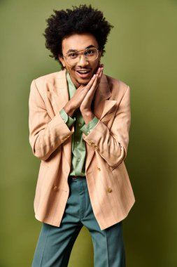 Genç, kıvırcık saçlı, şık bir takım elbise, kravat ve güneş gözlüğü takmış Afro-Amerikan bir adam yeşil arka planda bir portre için poz veriyor..
