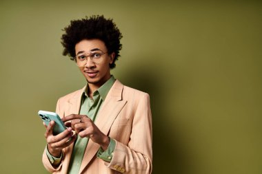 Takım elbiseli ve güneş gözlüklü şık bir Afrikalı genç adam, yeşil arka planda cep telefonuyla emilmiş..