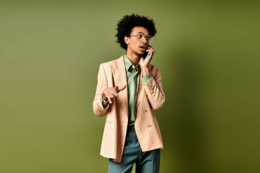 Takım elbiseli ve güneş gözlüklü şık bir Afrikalı genç Amerikalı cep telefonuyla canlı yeşil bir arka planda konuşuyor..