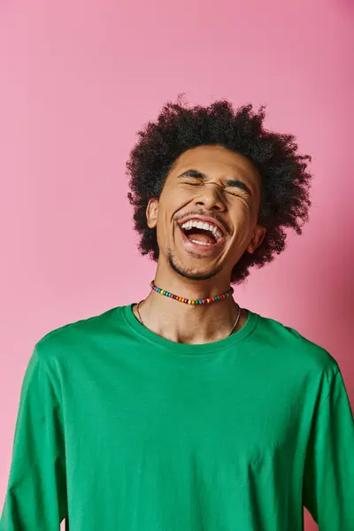 stock image A cheerful young African American man with a curly afro laughs while wearing a green shirt on a pink background.