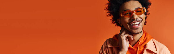 Молодой афроамериканец в оранжевой рубашке и солнцезащитных очках, делающий смешное лицо, демонстрирующий свои яркие эмоции.