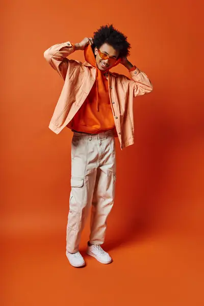 stock image Curly African American man in trendy orange shirt and khaki pants, exuding style and charisma on a bold orange background.