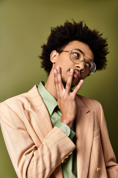 Стильный, молодой, кудрявый афроамериканец в костюме и очках делает глупое лицо на зеленом фоне.