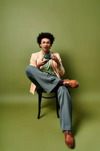 Стильный Афроамериканец Вьющимися Волосами Сидящий Стуле Держа Мобильный Телефон Одетый — стоковое фото