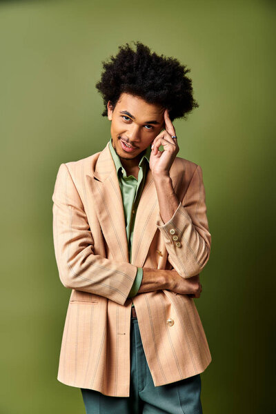 Young African American man in tan suit, green shirt against a green background.