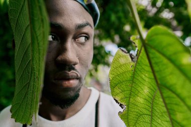 Sofistike bir Afrikalı Amerikalı, yemyeşil bir bahçede canlı yeşil bir yaprağın yanında şık bir şekilde poz verir..