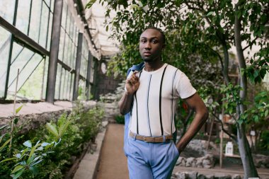 Handsome African American man in sophisticated white shirt and blue pants posing in a vivid green garden. clipart