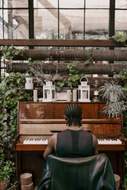 A man sits at a piano, playing in greenhouse. clipart