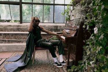 Entellektüel bir adam canlı yeşil bir bahçede kuyruklu piyanonun yanında oturuyor..