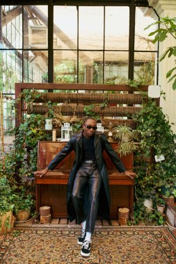 A stylish African American man sits gracefully on a piano in a room filled with vibrant plants. clipart