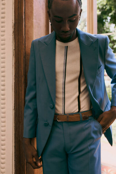 Handsome African American man in a blue suit standing stylishly next to a door.
