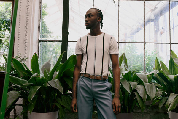 Изысканный афроамериканец стильно позирует в ярком зеленом саду.