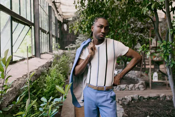 Stock image Handsome African American man in sophisticated dapper style, wearing a white shirt and blue pants, posing in a vivid green garden.