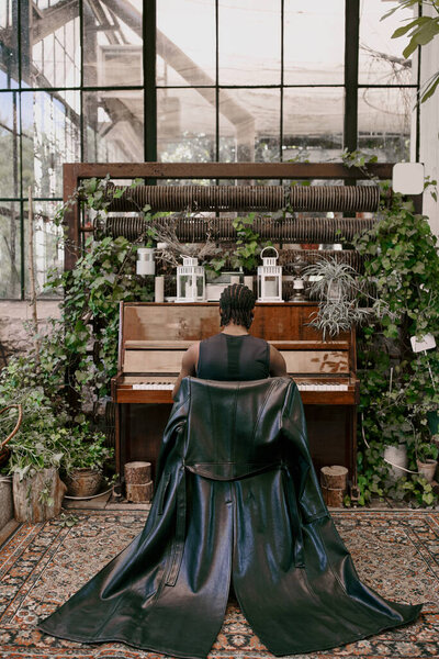 A man plays the piano in a verdant greenhouse.