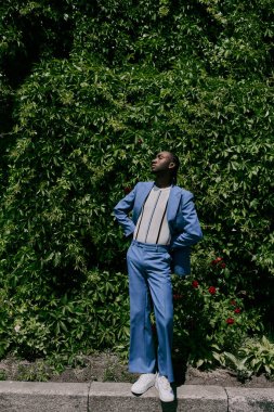 Mavi takım elbiseli şık bir adam kentin kaldırımında güven içinde duruyor..