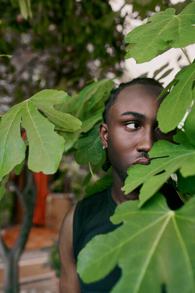 Красивый афроамериканец со сложным стилем, стоящий перед пышным зеленым деревом.