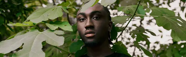 stock image A handsome African American man stands confidently in front of a lush, vibrant green forest.