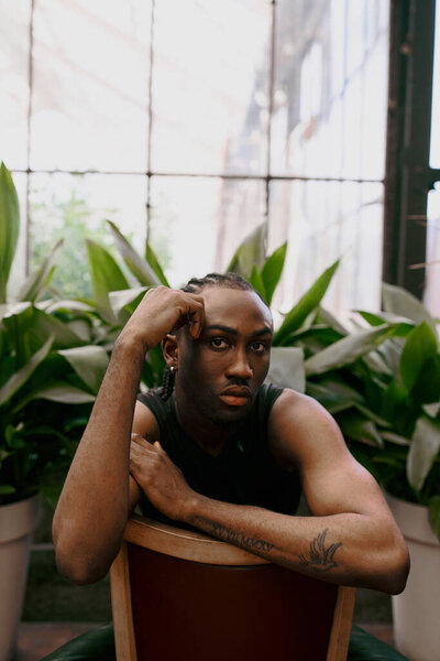 African American man in dapper style sits in chair, hands on head, deep in thought.