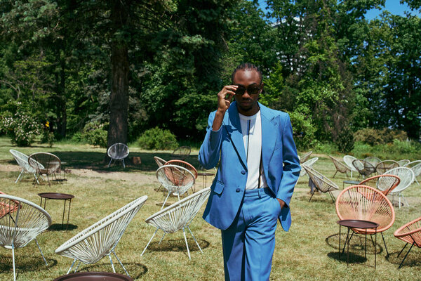 Красивый мужчина в синем костюме бродит по полю стульев в ярко-зеленом месте.