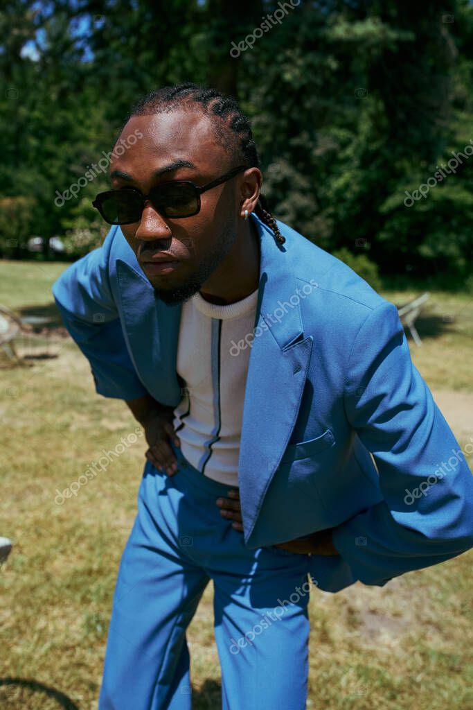Handsome African American man with dapper style poses in vivid green garden.