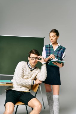 Handsome man and gorgeous woman posing together by a green board in a college setting. clipart
