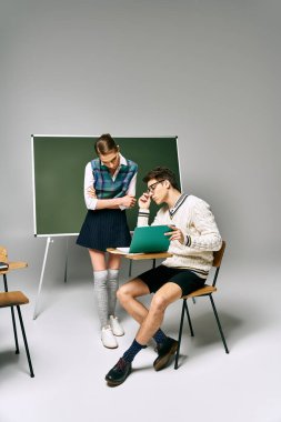 A man and a woman sit in front of a green board at college. clipart