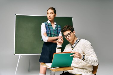 A handsome man and a beautiful woman sitting in front of a green board in a college setting. clipart