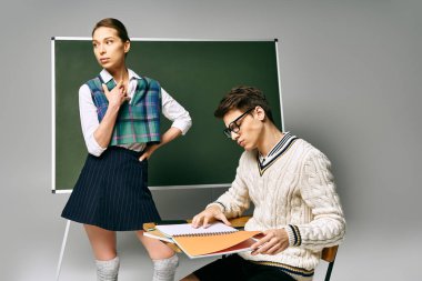 A stylish man and woman sitting by a green board in a college setting. clipart