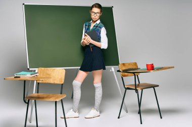 Okul üniformalı bir kız öğrenci yeşil bir kurulun önünde duruyor..
