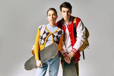 Genç öğrenciler gri zemine karşı kaykaylarla rahatça poz veriyorlar.