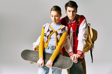 Gri arka planda kaykayla poz veren şık giyinmiş genç öğrenciler..