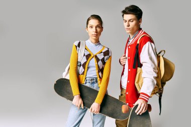 Gri bir zeminde kaykay tutan iki genç insan..