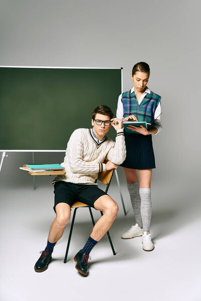 A man and a woman posing elegantly in front of a green board in college.