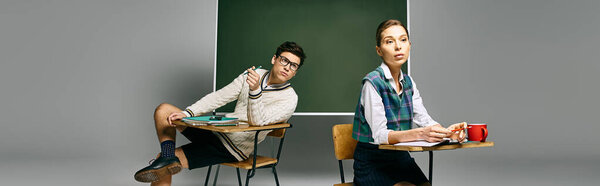 Two elegant students sit at a desk in a college classroom, engaging with a green board.