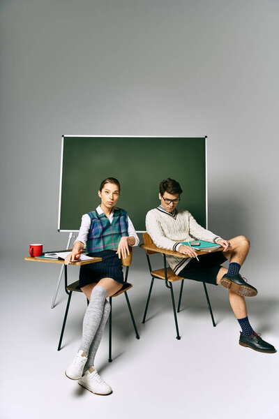 Young man and woman sitting elegantly in front of a green board in a college setting.